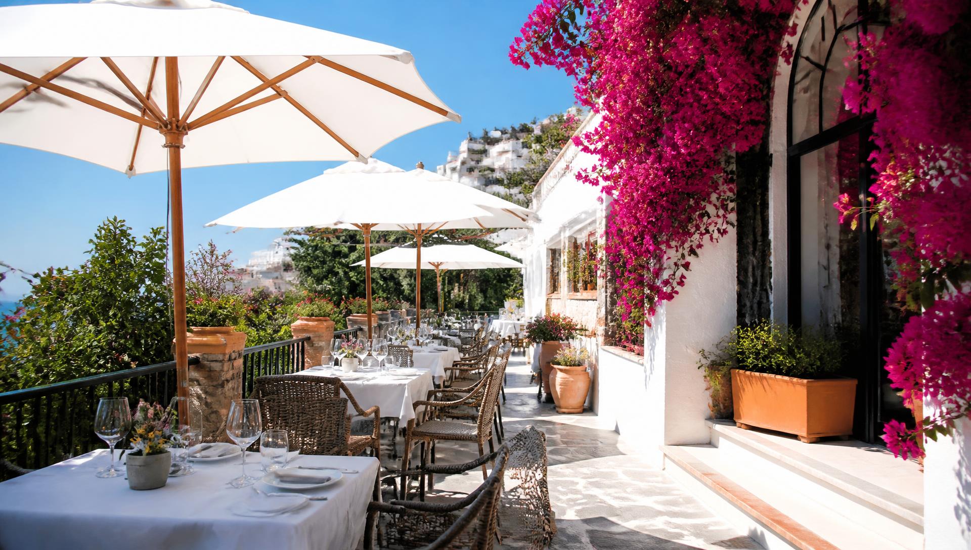 Senza Fretta summer terrace at midday, white parasols above set tables under a blue sky